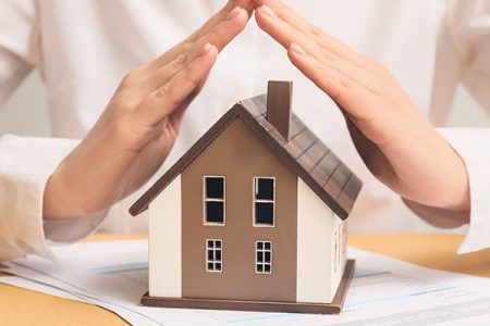 Woman with house model on color table, closeup. Property insuran